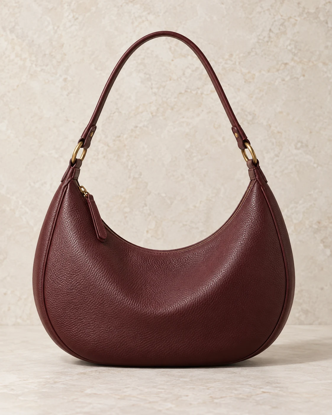 An oxblood crescent leather shoulder bag with brass fittings